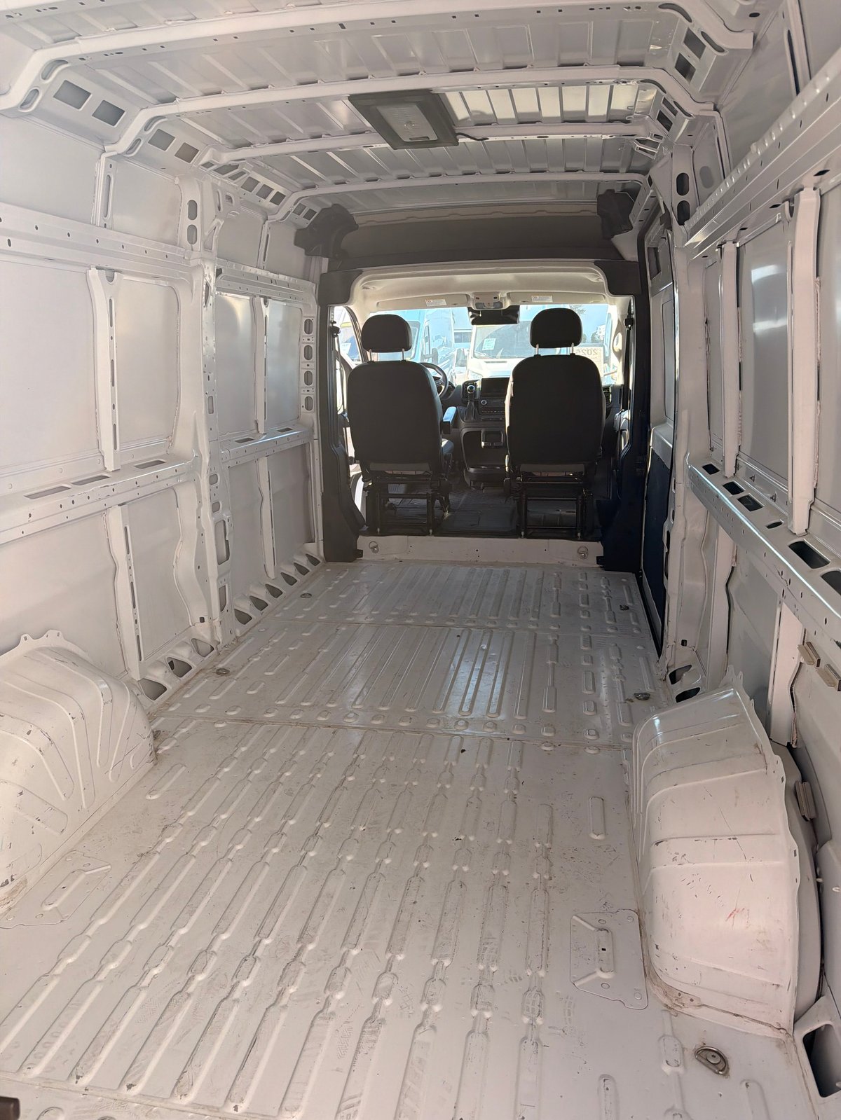 Interior view of empty white commercial van with ribbed metal cargo floor and front cab visible