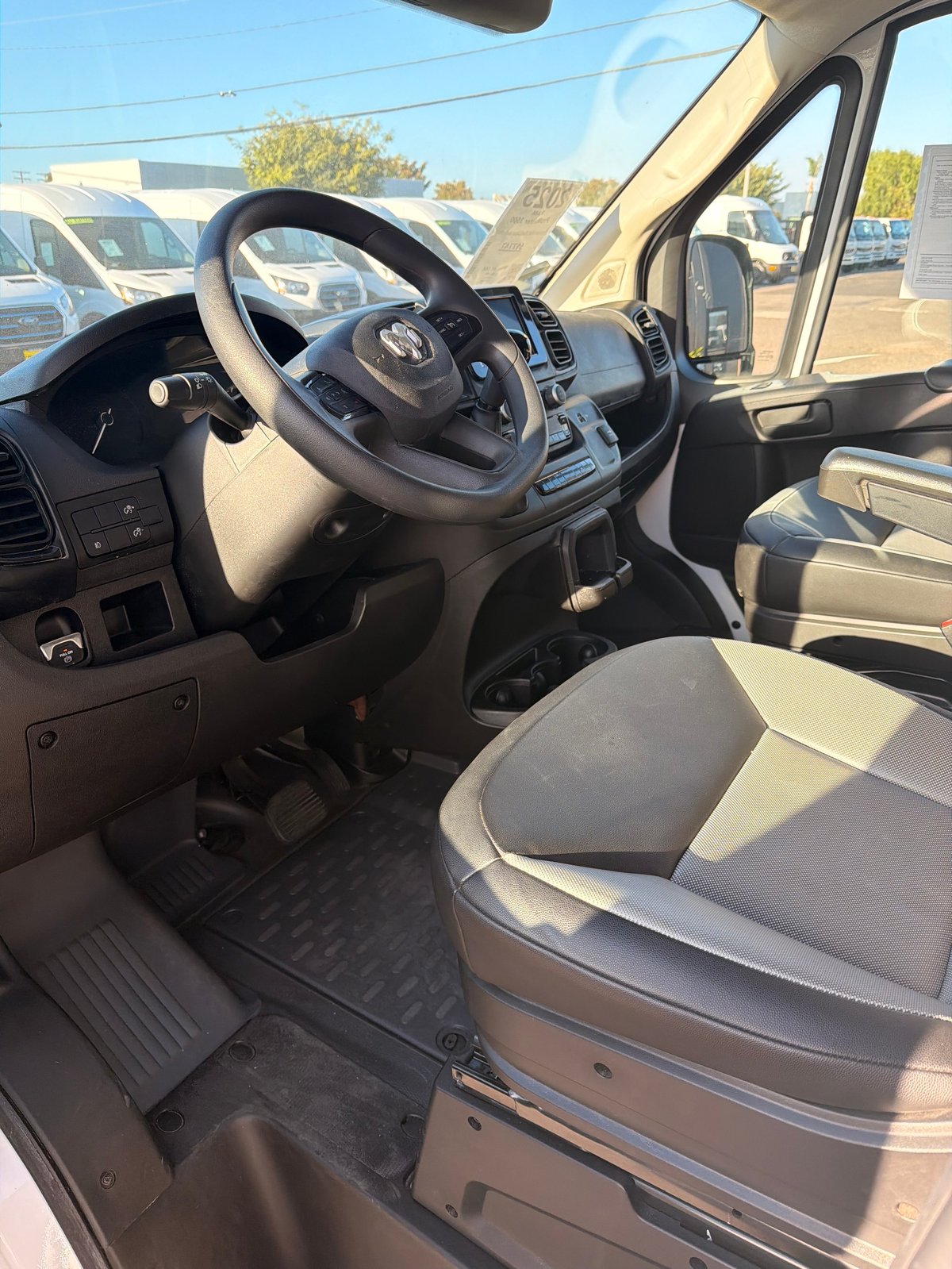 Interior view of a commercial vehicle showing steering wheel, dashboard, and two-tone seats with parking lot visible through windshield